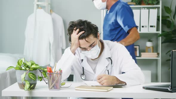 Young Tired Doctor Working at Hospital Elderly Surgeon Greeting Colleague Male Therapists Wearing alt