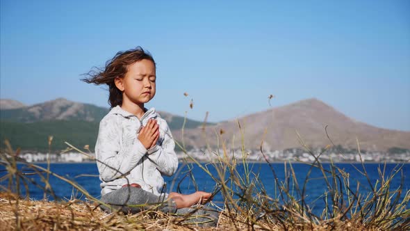 Cute Little Child Gurl Meditating Alone in Lotus Pose at Lake Shore alt