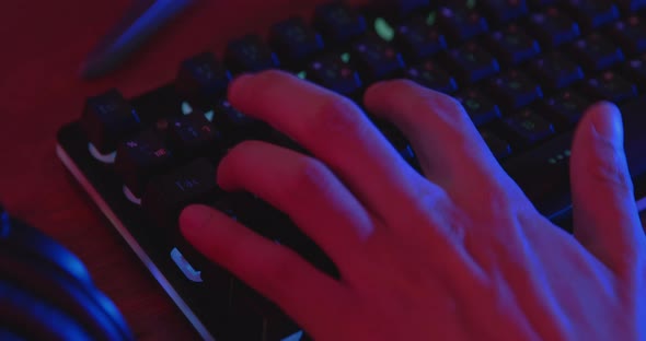 Hand of young gamer playing e-sports pressing on computer keyboard at night