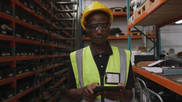 African American male factory worker at a factory wearing a high vis vest using a tablet computer alt
