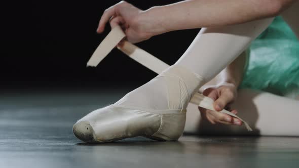 Unrecognizable Girl Ballerina Dancer Sits on Floor in Dance Class on Stage Puts on Pointe Shoes Ties alt