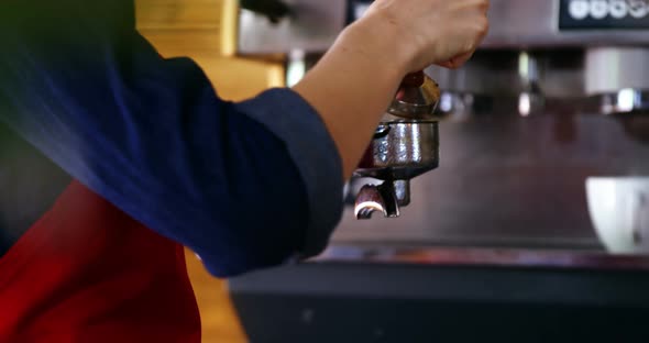 Waitress using a tamper to press ground coffee into a portafilter alt