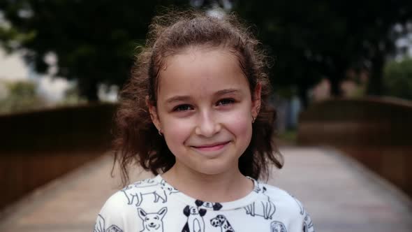 Portrait Little Happy Child Girl Looking at Camera Standing on Street in City on Summer Day alt