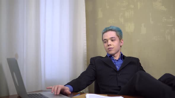 Young Happy Businessman Looking at Laptop Put Legs on the Work Desk Smiling