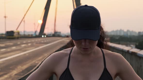 Young Motivated Girl is Preparing to Run on City Bridge During Sunset alt
