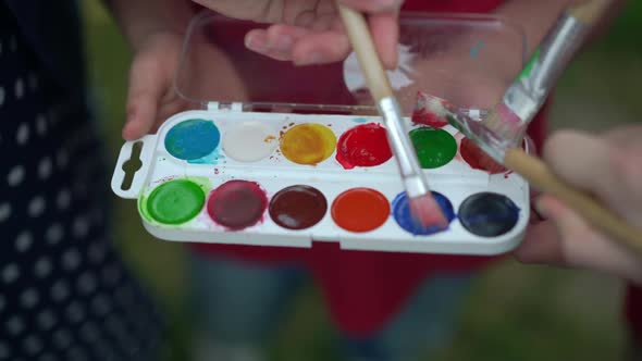 Closeup Painting Palette with Children Hands Coloring Brushes in Slow Motion alt