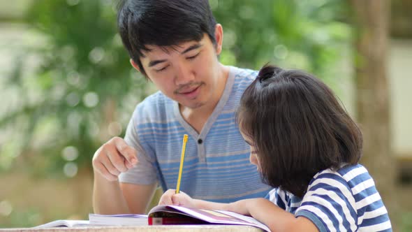 Little Asian girl with father doing homework on the table. alt