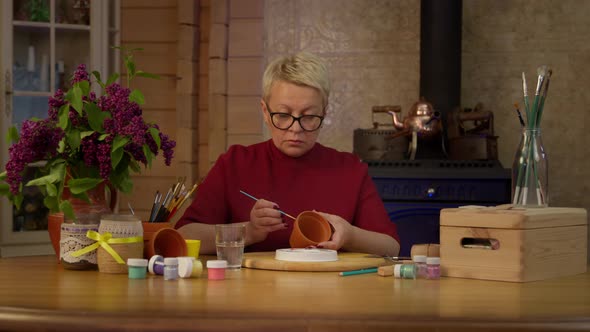 Focused Female Artist Paints Surface of Clay Pot with Paintbrush in Workshop alt