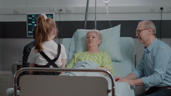Retired Woman Enjoying Visit From Little Girl and Mother in Hospital Ward alt