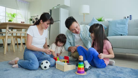 Asian happy family sit on floor, play with little kid daughter together in living room in house. alt