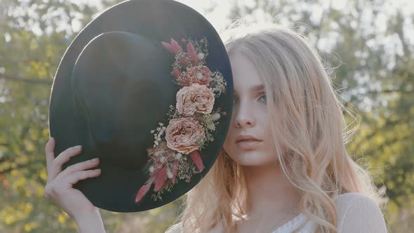 Young beautiful blonde in a white dress posing with a dark hat. Attractive fashion model with loose  alt