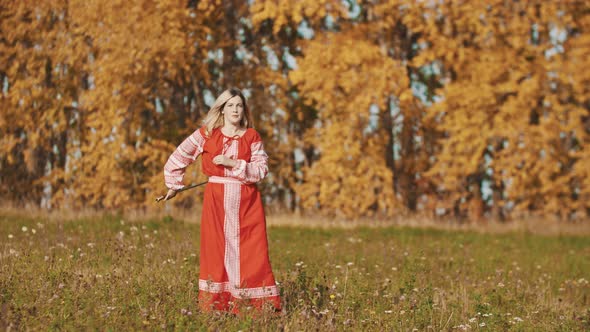 Woman in Red Traditional Dress Standing on the Field and Fencing with a Sword alt