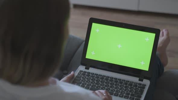 Woman at Home Sitting on a Couch Corks on a Laptop Computer with Green Mock-up Screen. Girl Using alt