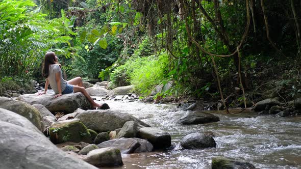 A young asian woman relaxing and sitting on the rocks by the waterfall