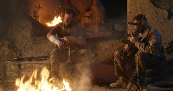 Soldiers Tending Wounds and Checking Rifle Near Campfire alt