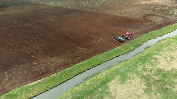Farmer on a Tractor Cultivates Farmland with a Disc Harrow Near a Small Reclamation River alt
