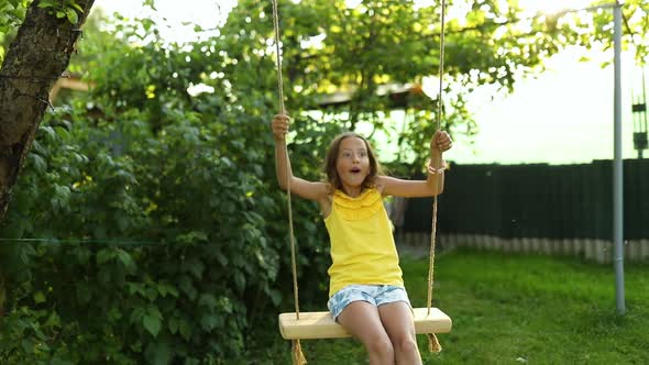 Happy barefoot laughing child girl swinging on a swing in sunset summer day