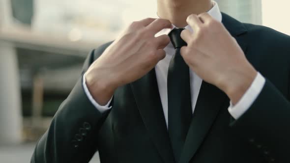 Close up of Asian businessman getting dressed in a black suit preparing for work.