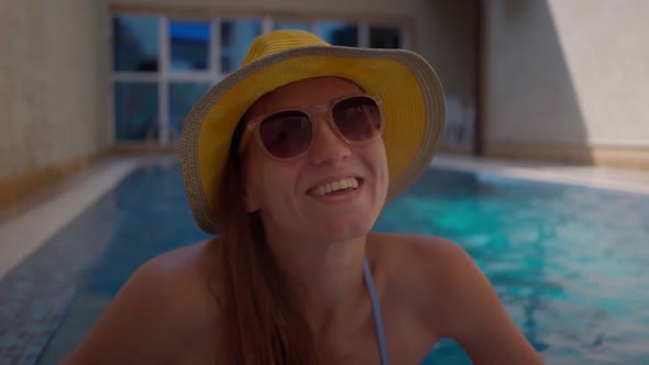 a Young Beautiful Girl in a Yellow Hat and Sunglasses is Relaxing in the Pool and Smiling
