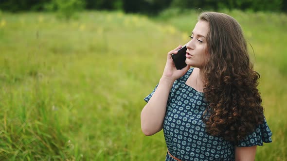 Serious Young Caucasian Woman Speaks at Mobile Phone at Sunny Windy Weather