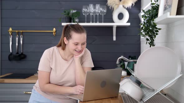 Woman Stands in the Kitchen and Communicates Via Video on Laptop alt