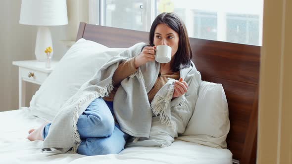 Thoughtful woman wrapped in blanket having coffee 4k alt