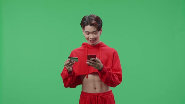 Transgender Male Using Mobile Phone With Credit Card For Shopping Online In The Green Screen Studio alt