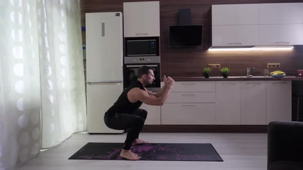 The Athlete Performs an Exercise on His Feet and Buttocks in the Home Kitchen