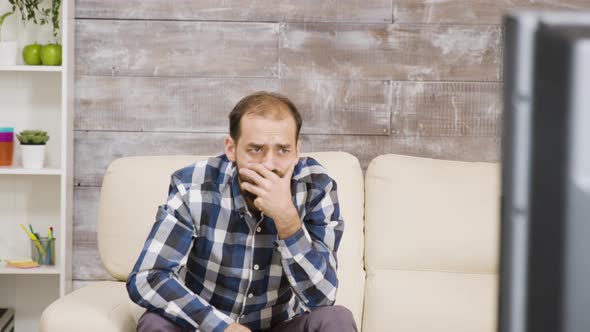 Bearded Man Sitting on Sofa with Shocked Expression alt