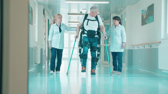 Medical Workers are Helping a Disabled Man to Walk in the Exosuit alt