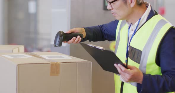Asian male worker wearing safety suit and scanning boxes in warehouse alt