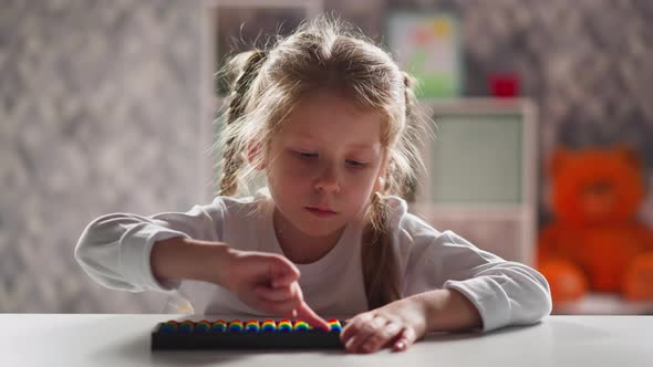 Little Kid with Blonde Plaits Touches Abacus By Finger alt