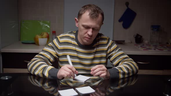 Man Writes on Stickers His Plans for the Future Sitting at the Table in the Evening Planning Things alt
