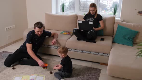 Little Boy is Playing with His Father While His Mother Works Using a Notebook alt