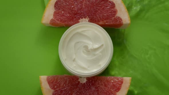 Water Flowing Slow Mo on Jar of Beauty Cream with Open Lid and Grapefruit Slices