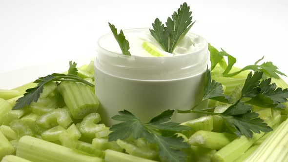 Jar of a natural celery-infused cream, and fresh celery stalks, background