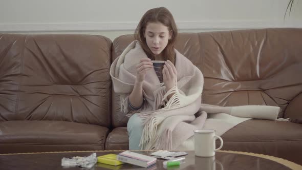 Portrait Small Sick Girl Sit in the Sofa, Tablets, Pills and Cup on the Table alt