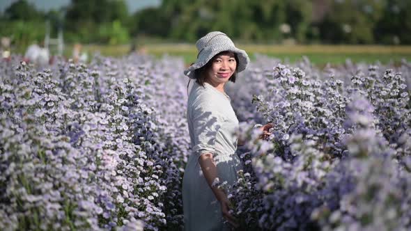 Asian woman walking in a flower garden and looking back at the camera, slow motion.