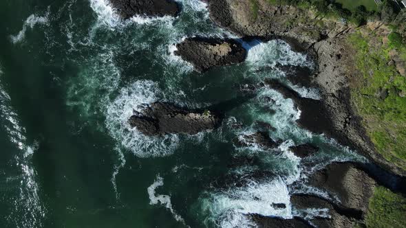 High view of waves breaking over a towering volcanic rock ledge on a coastal headland. Drone view alt