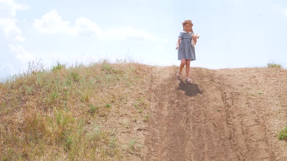 Adorable little girl in vintage dress and straw hat running down the hill and laughing