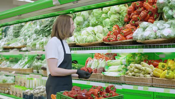 Man Replenishes Products on the Shelves Juggles Red Pepper Fruits Young Man Puts Paprika on a Shelf alt