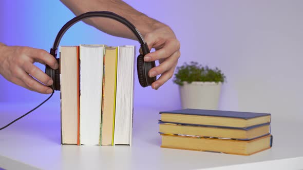 Black headphones with stack of books on blue background. Audio books or education concept. alt