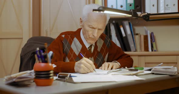 Senior Businessman Writing on Paper at Table in Office alt