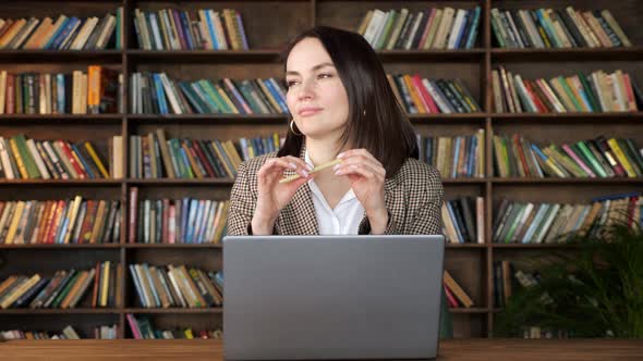 Thoughtful Brunette in Jacket Over White Blouse Holds Pen alt