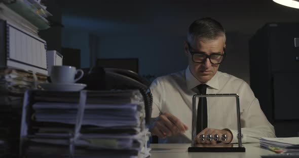 Sad office worker sitting at desk and staring at Newton's cradle balls