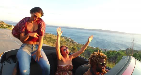 Beautiful brunette sitting on hood of convertible while riding with her friends alt