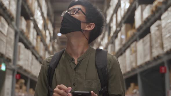 Asian man wearing mask walking in warehouse and use smart phone.