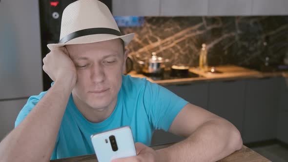 Man in White Hat Sits at the Table Uses Mobile Phone alt
