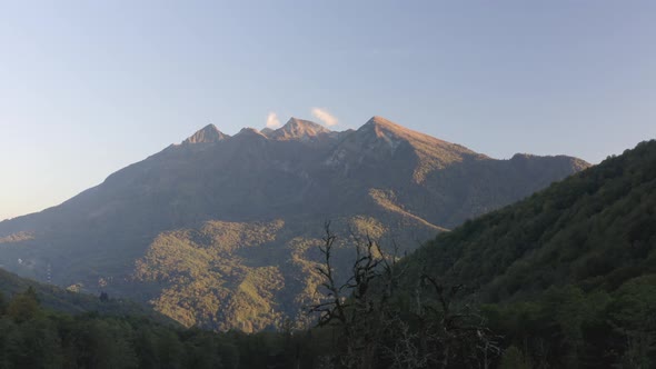 Shooting From Helicopter Natural High Mountain Covered By Dense Green Forest Treetops at Sunrise alt