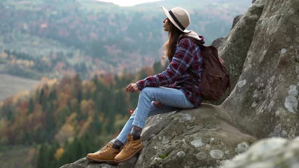 Woman Hiker in Hat Sits on Edge of Cliff and Looks Into Distance Mountain View Travel and Sports alt